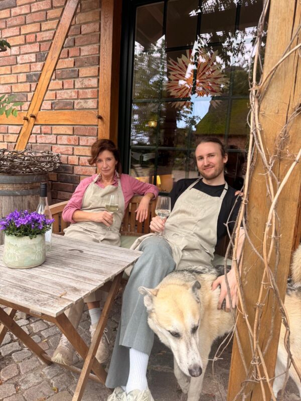 Ella und Linus in Werkstattschürzen mit einem Hund vor dem Fachwerkhaus auf Gut Moor