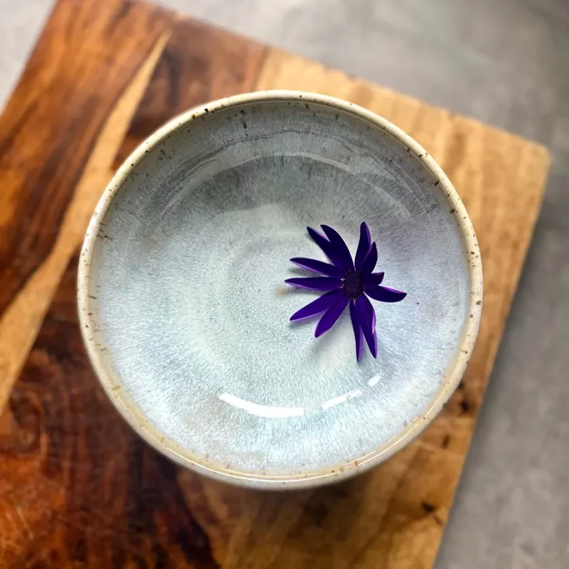 Glasierte Keramikschale mit einer violetten Blüte auf einer Holzfläche